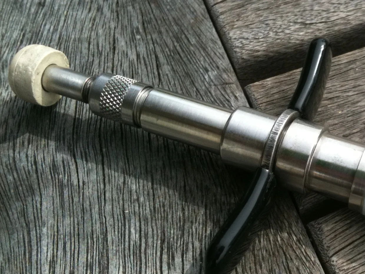 Close-up of a handheld chiropractic adjusting instrument: a cushioned stylus tip, a knurled adjustment collar and a steel barrel